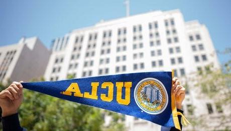 加州大学洛杉矶分校(UCLA)位于洛杉矶市中心的信托大楼，前景中有双手举着一面三角旗